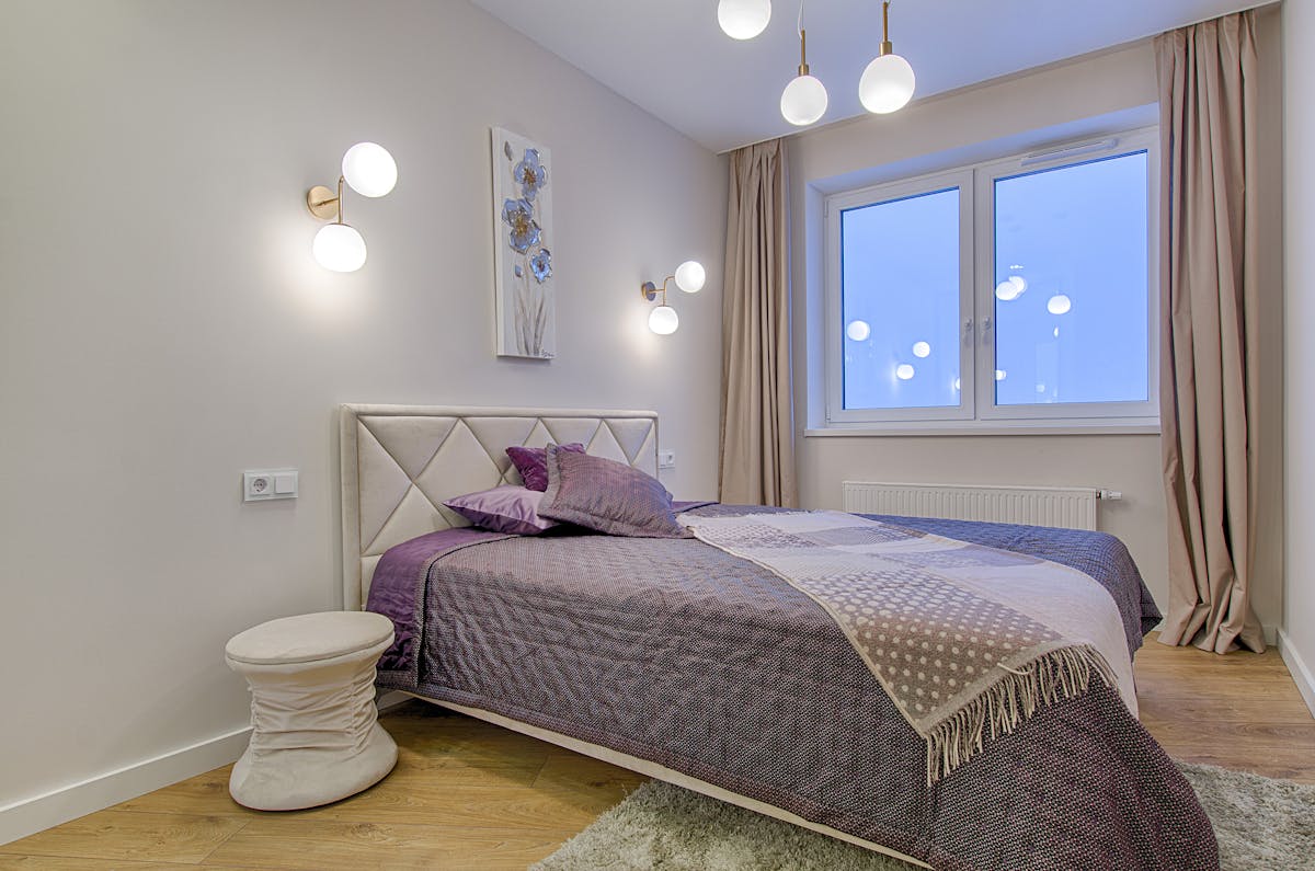 A warmly lit small bedroom with curtains and wall sconces