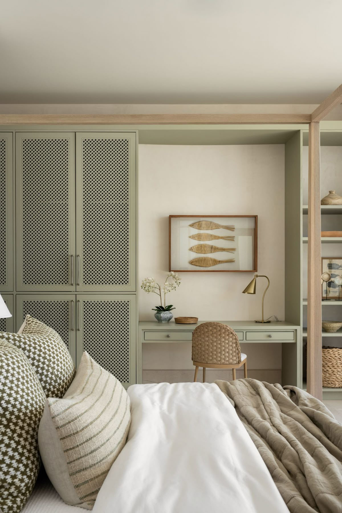 A calm, spare bedroom with white walls, a low bed with neutral linen, and a narrow wooden dresser tucked beside a window casting soft morning light